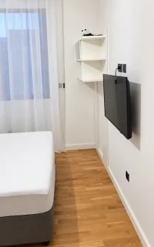 Svjetla spavaća soba sa krevetom, prozorom i zidnim televizorom. - image 6