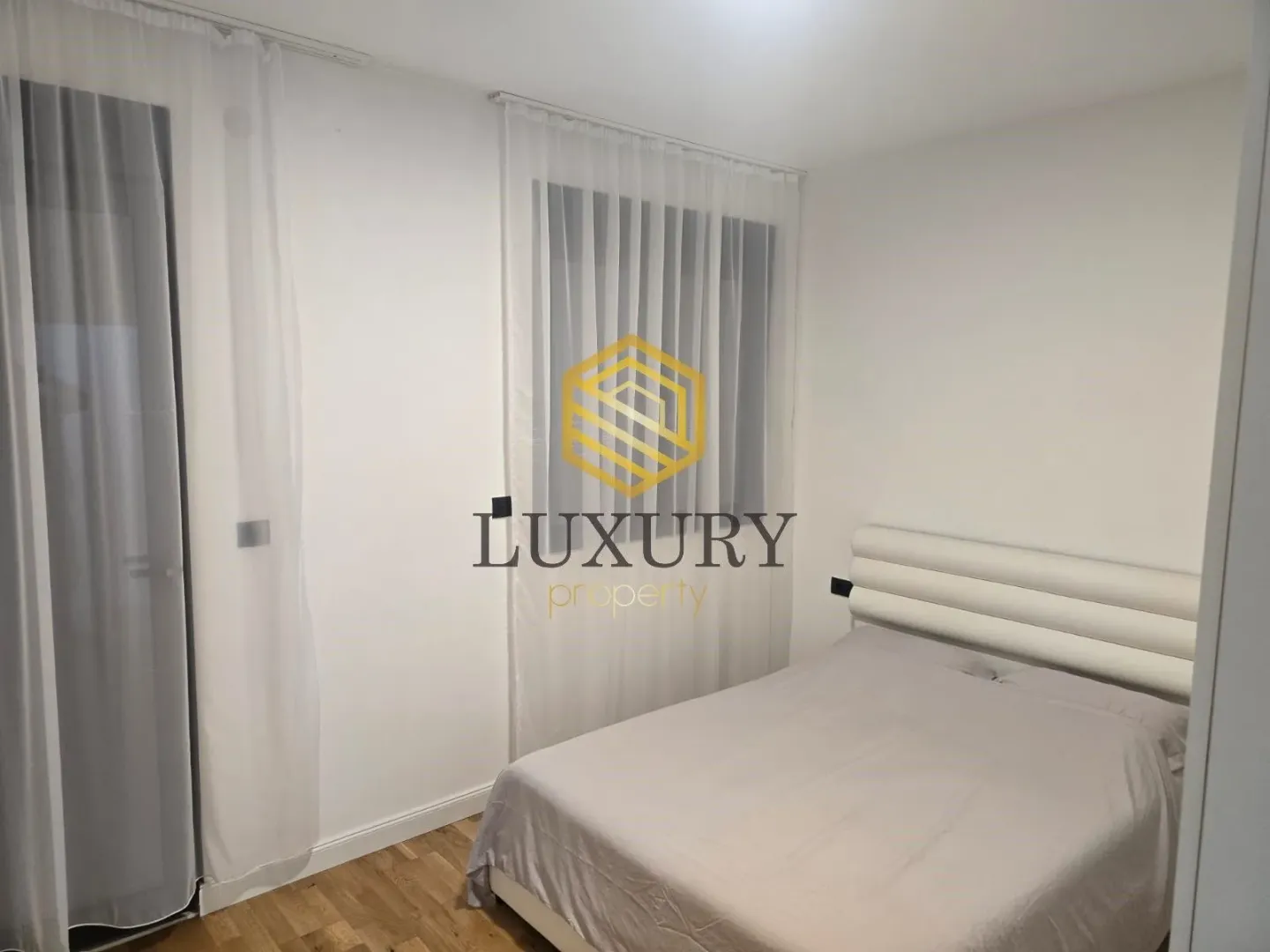 Bright bedroom with a double bed and white curtains.