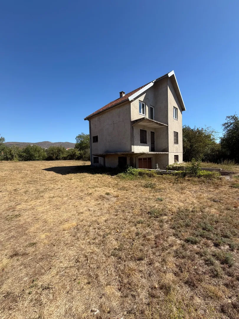 Pogled na spoljašnjost kuće sa dvorištem i okolnim rastinjem.