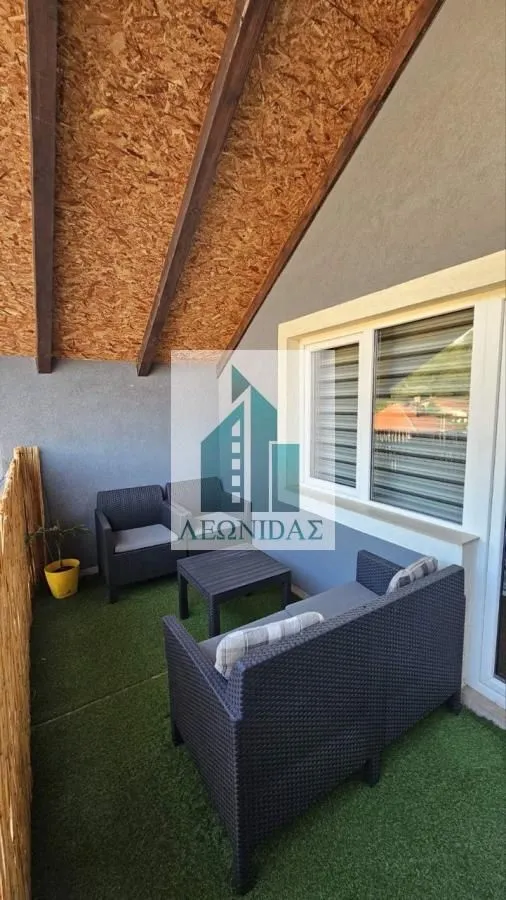 Covered balcony with outdoor seating furniture and artificial grass on the floor.