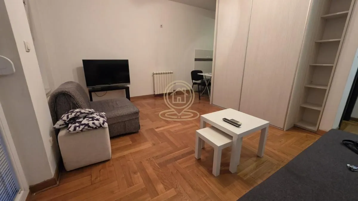 Dnevna soba sa garniturom, televizorom i drvenim podom.