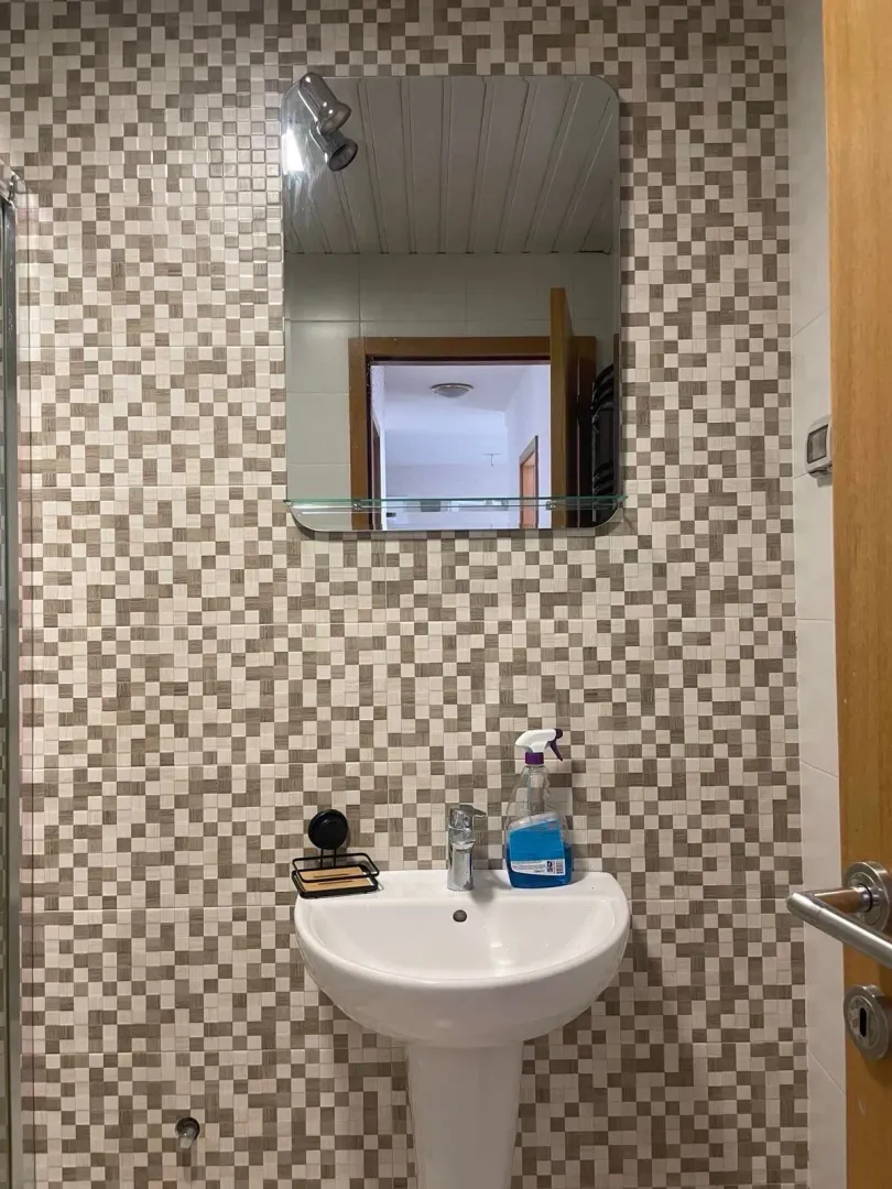 Small bathroom with a sink and mirror on a mosaic-tiled wall.