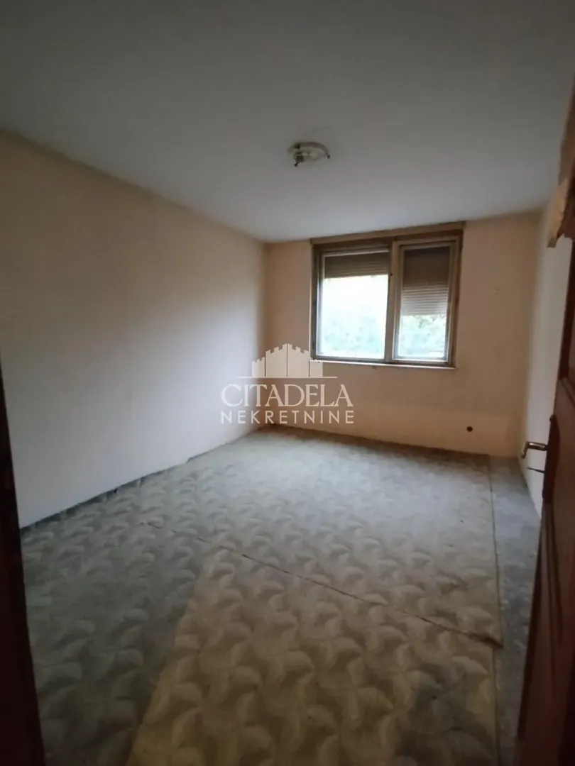 Prazna prostorija sa prozorom i starim tepihom.