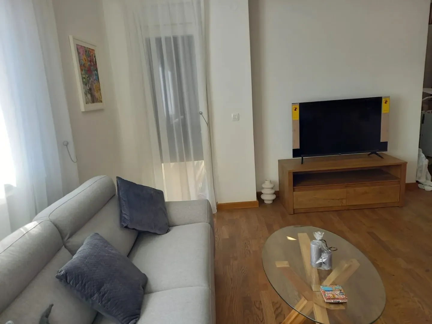 Bright living room with a sofa, TV unit, and glass coffee table.