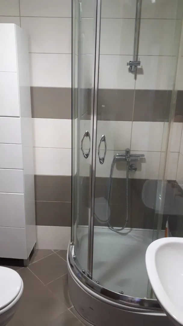 Kupatilo opremljeno tuš kabinom, umivaonikom i bijelim ormarićem.
