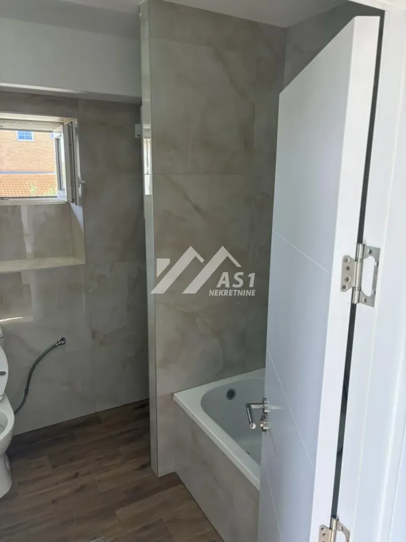 Tiled bathroom with a bathtub and a window.