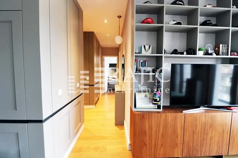 Living room with a TV, shelving unit, and a hallway passage.