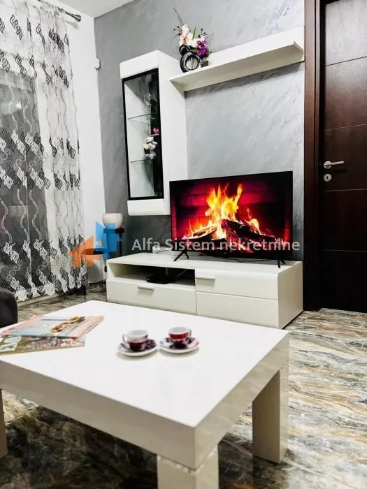 Dnevni boravak sa televizorom, belim komadnim nameštajem i stočićem.