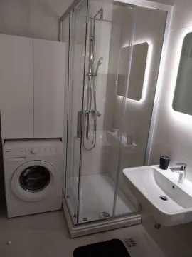Modern bathroom with a shower cabin, sink, and washing machine. - image 11