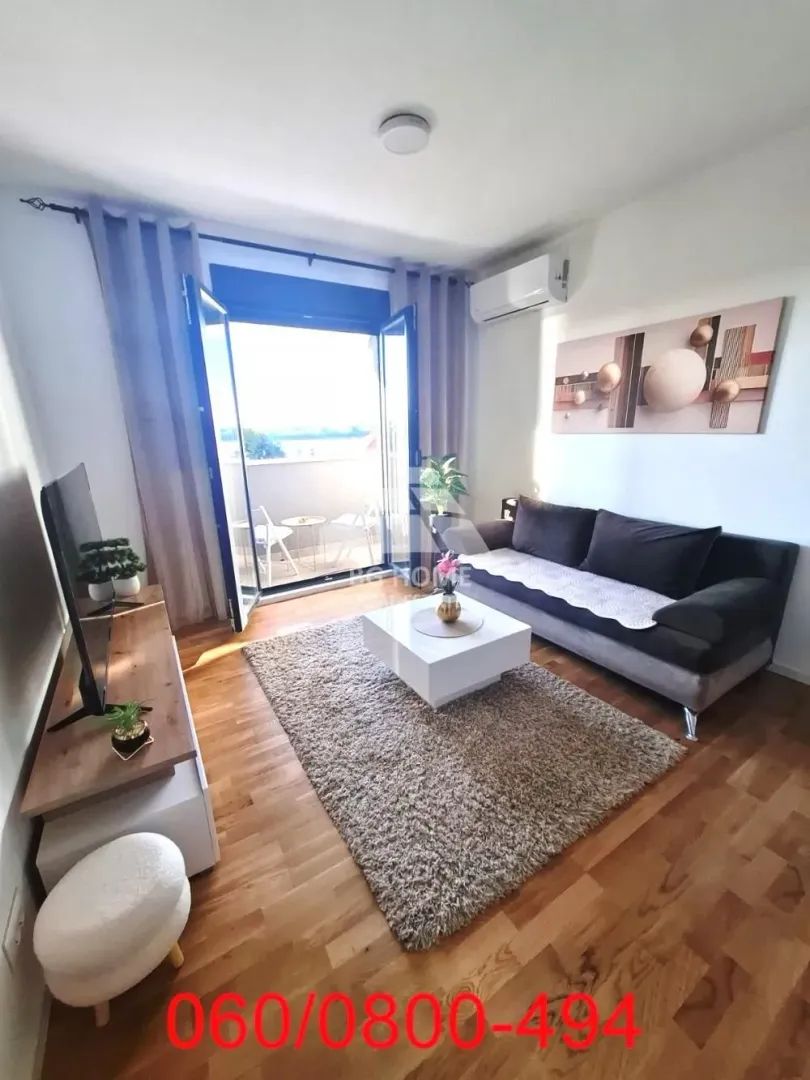 Dnevna soba sa garniturom, TV komodom i izlazom na terasu.