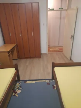 Jednostavna spavaća soba sa dva kreveta, velikim drvenim ormarom i radnim stolom. - image 6