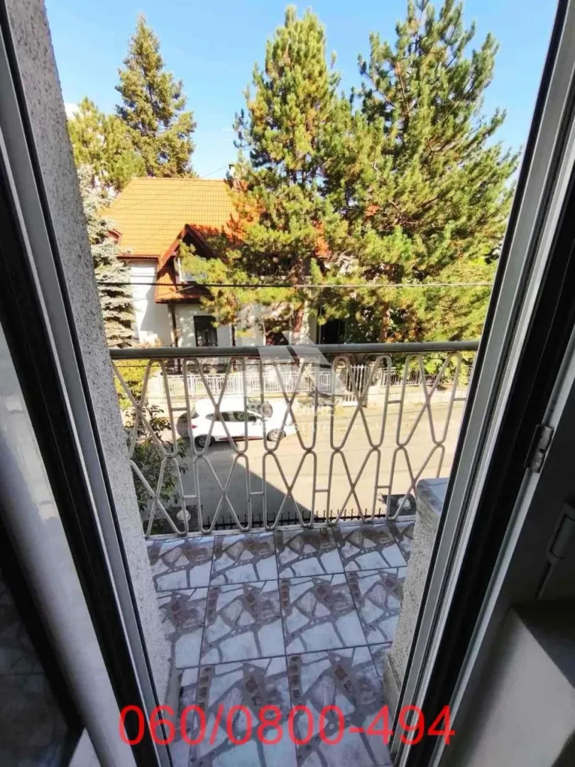 Pogled sa balkona na dvorište i okolno zelenilo.