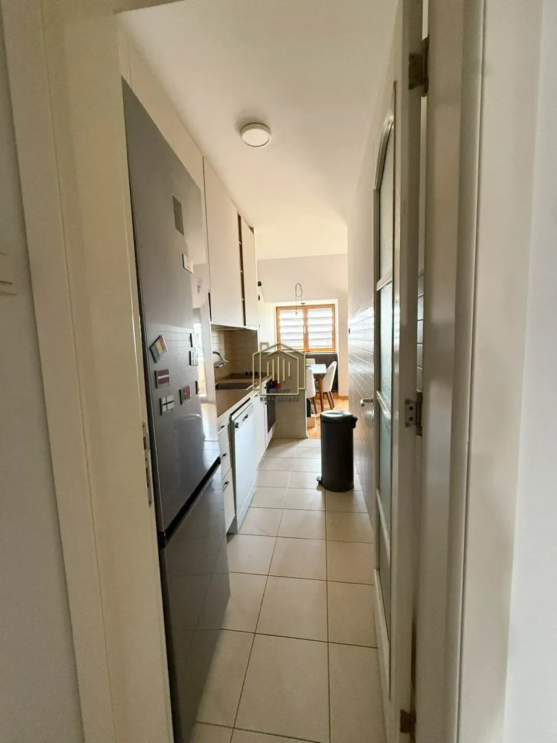 View from the hallway into a narrow kitchen with white cabinetry and a refrigerator.