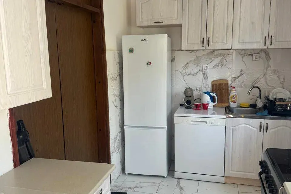 Small kitchen with white cabinets, refrigerator, and sink.