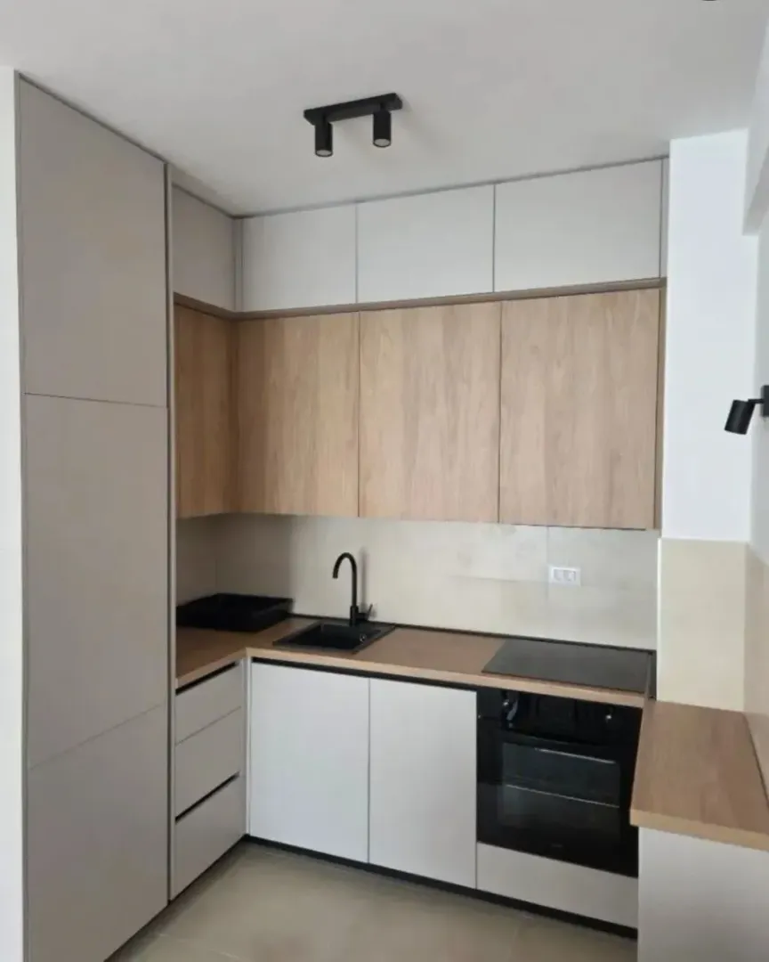 Modern corner kitchen in light tones with built-in appliances.