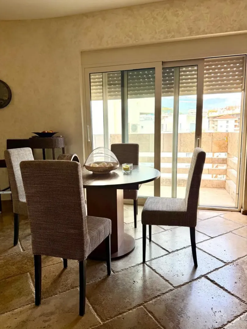 Dining area with a round table and chairs, next to glass doors leading to the terrace.