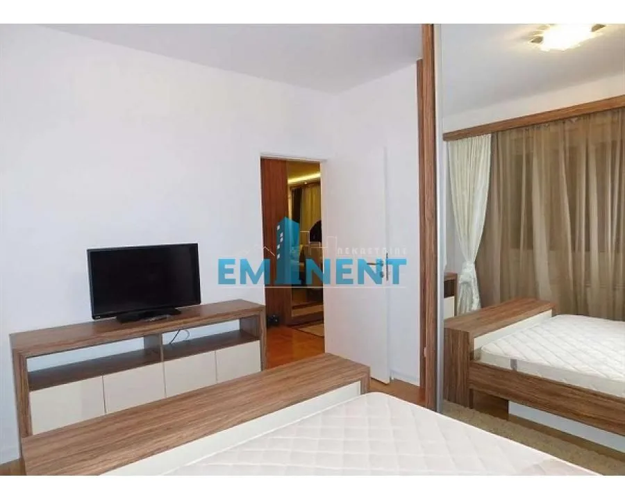 Furnished bedroom with a double bed, TV console, and a large mirrored wardrobe.