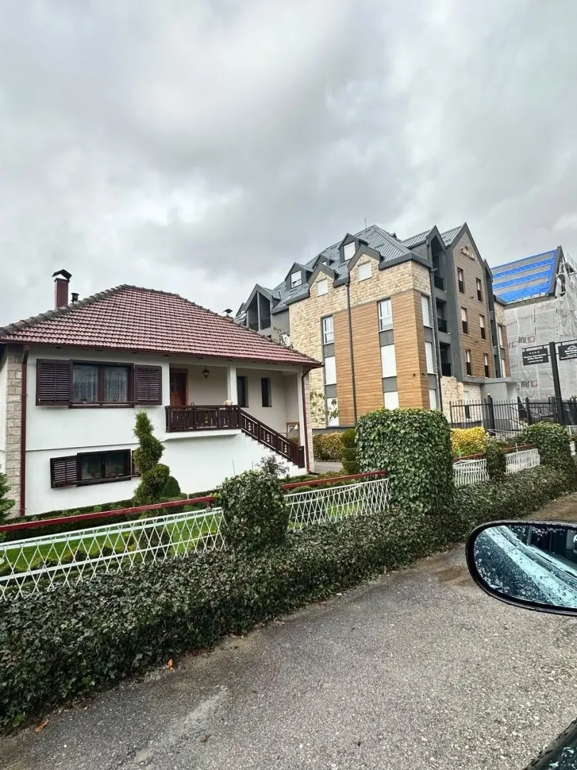 Pogled sa ulice na porodičnu kuću sa dvorištem i okolne zgrade.