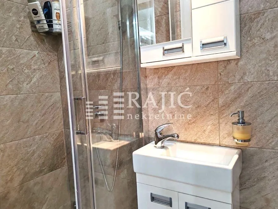 Small bathroom with a sink, shower cabin, and ceramic tiles.