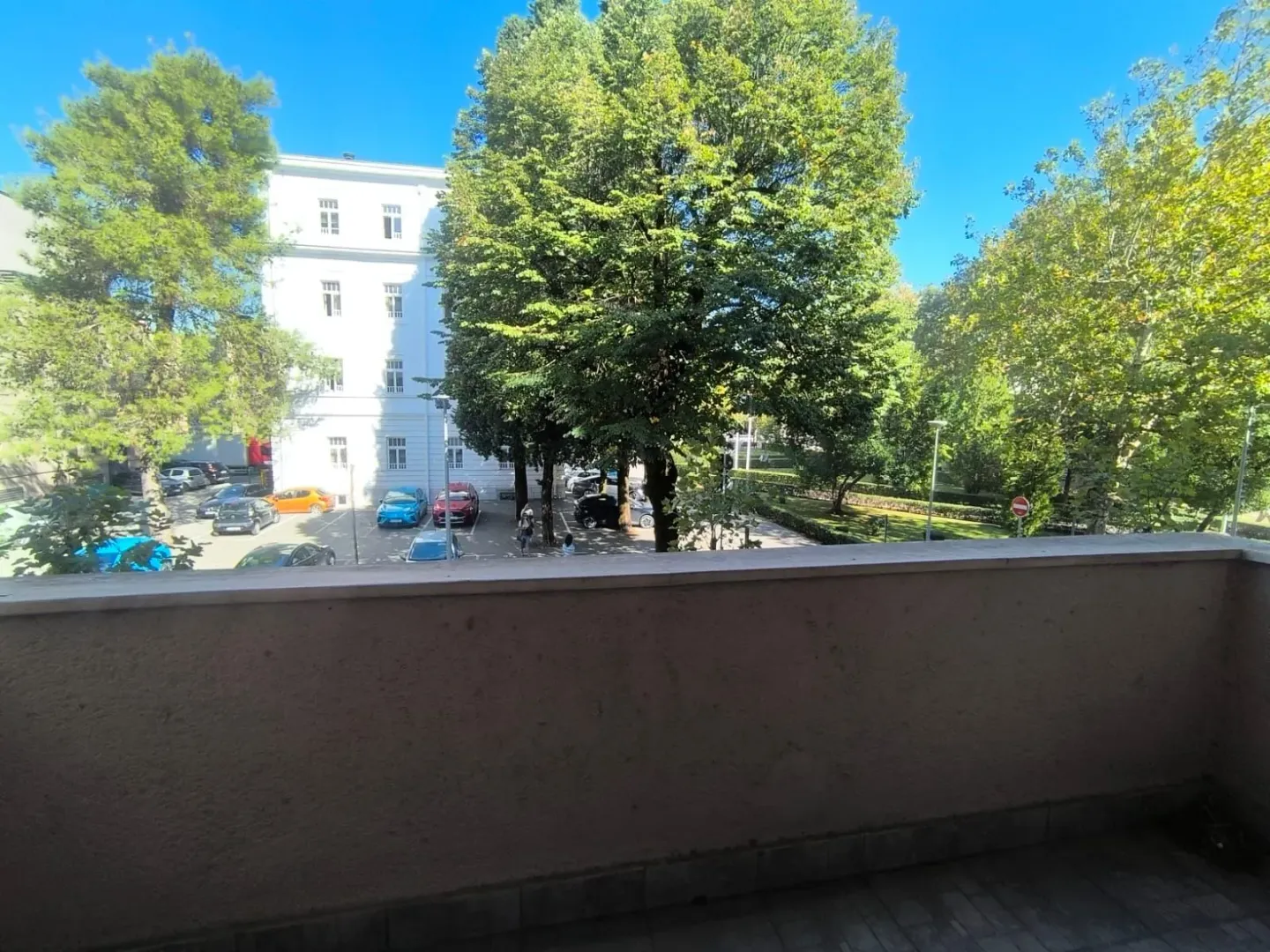 View from the balcony overlooking surrounding buildings, a parking lot, and greenery.