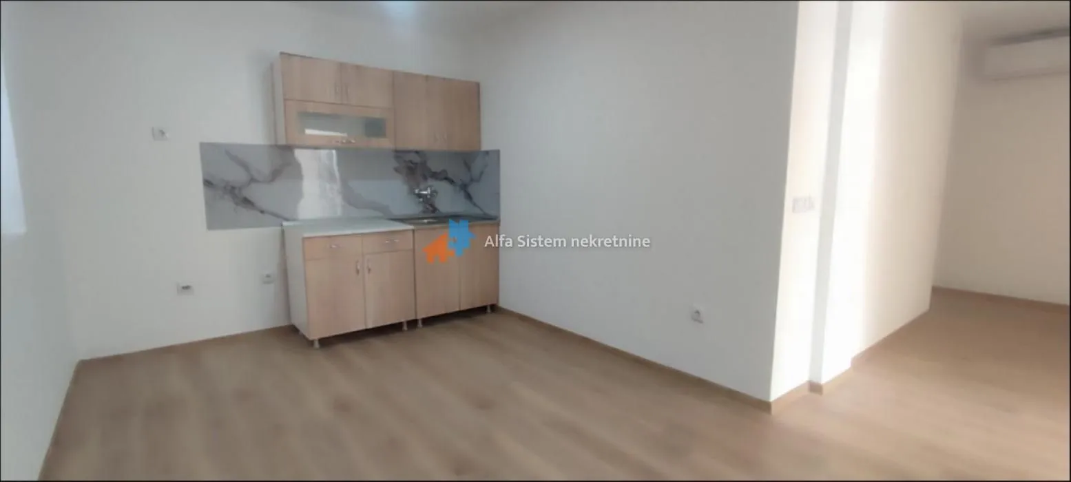 Small kitchen with wooden cabinets in a bright room with laminate flooring.