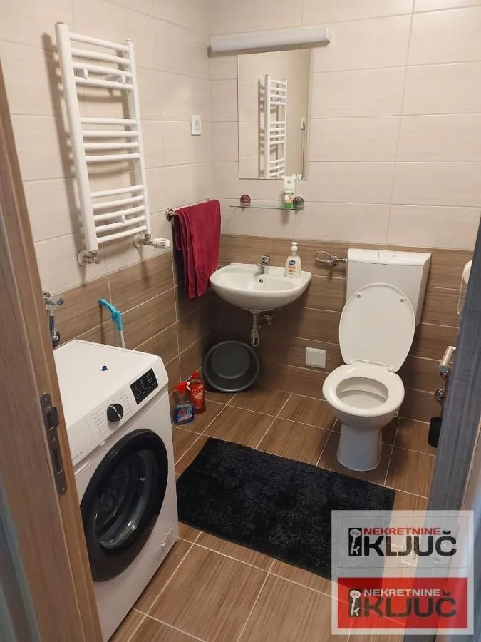 Kompaktno opremljeno kupatilo sa veš mašinom, umivaonikom i WC šoljom.