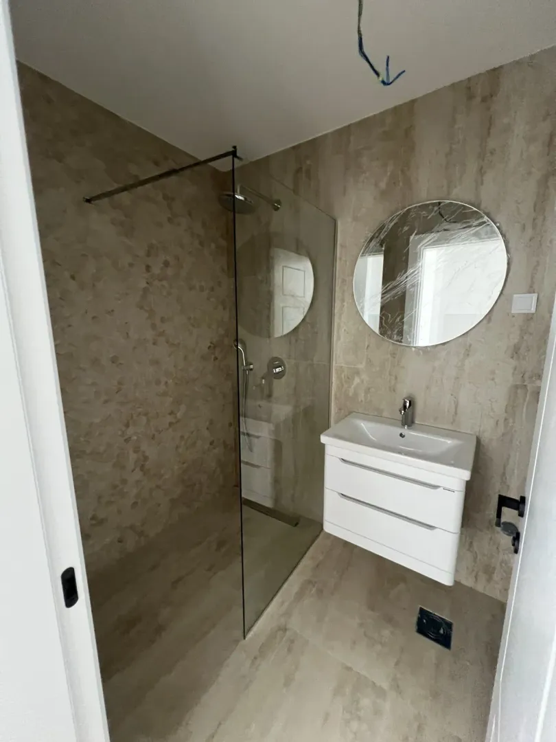 Modern bathroom with a walk-in shower, sink, and a round mirror.