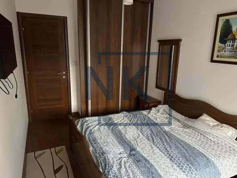 Namještena spavaća soba sa bračnim krevetom, velikim ormarom i drvenim vratima.