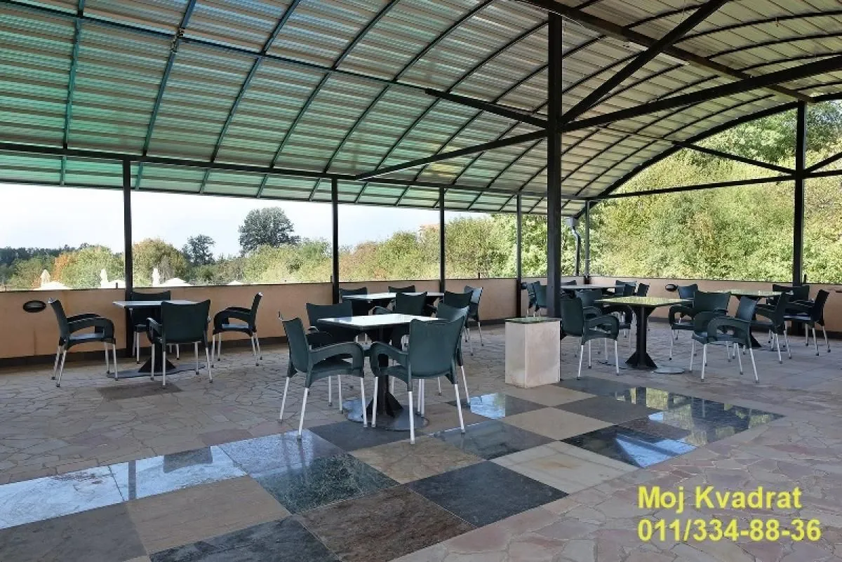 Large covered terrace with tables and chairs and a view of greenery.