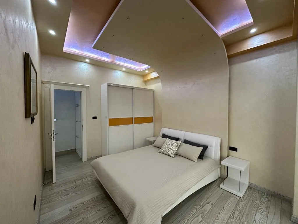 Furnished bedroom with a double bed, wardrobe, and a dropped ceiling with lighting.