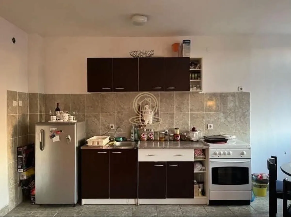 Manja kuhinja sa tamnim elementima, frižiderom i šporetom.