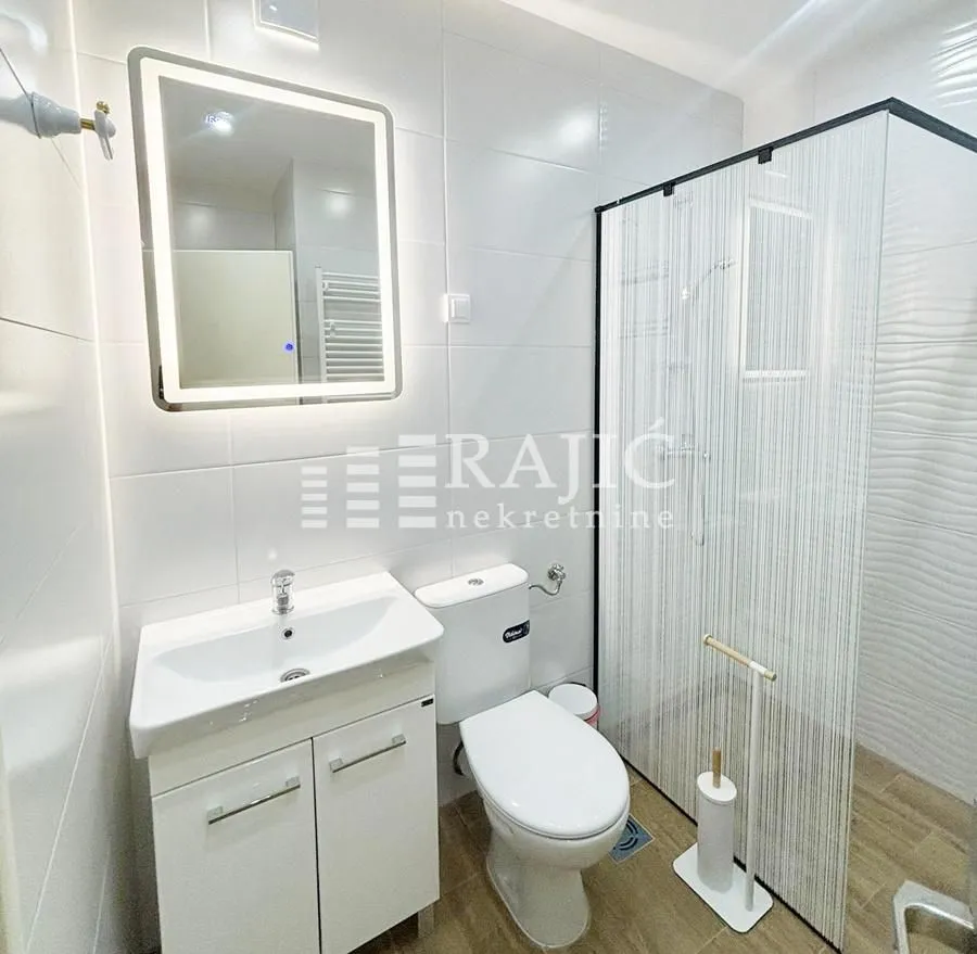 Modernly equipped bathroom with white tiles, walk-in shower, and sink.