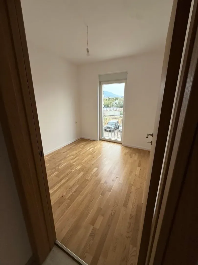 Prazna soba sa drvenim podom i izlazom na balkon.