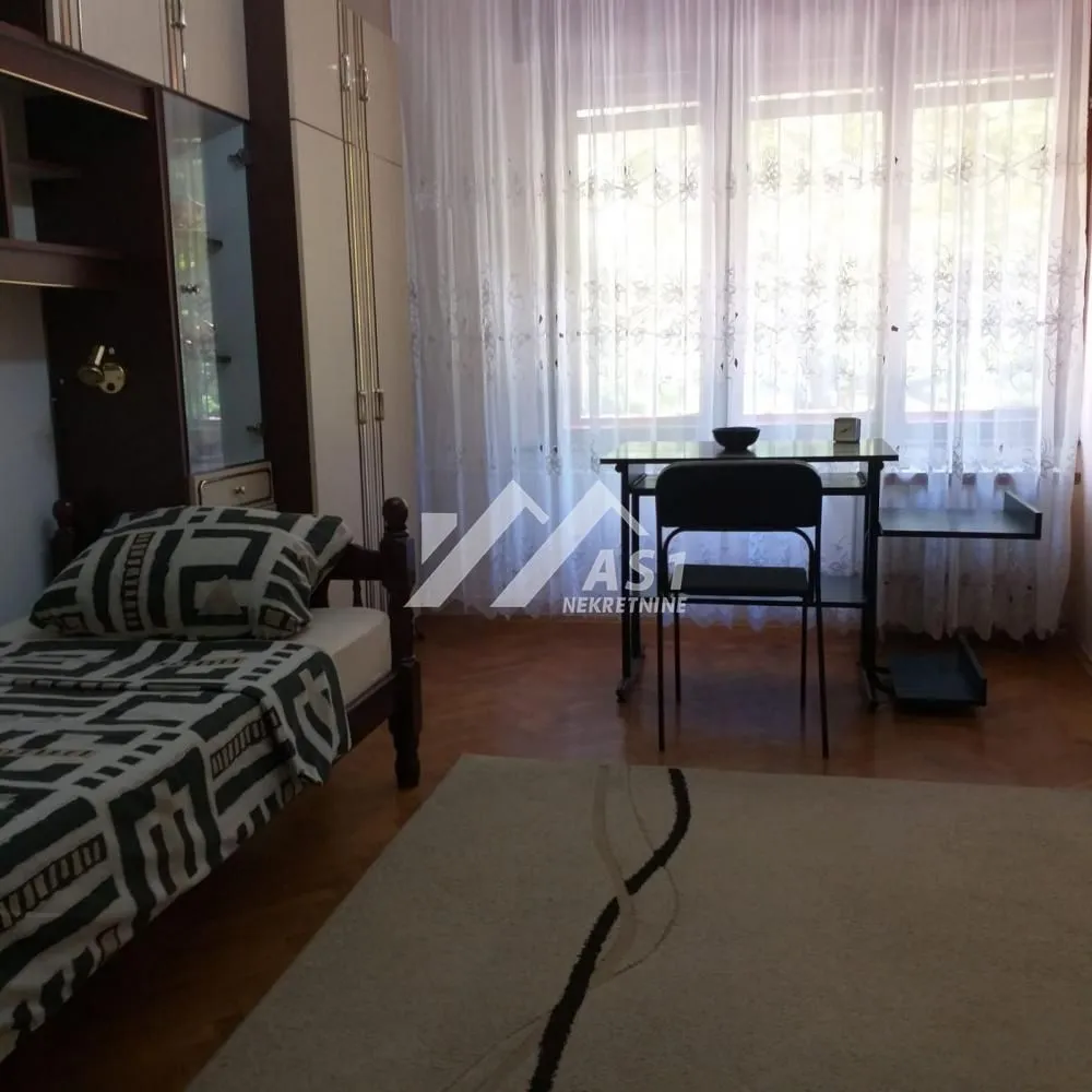 Nameštena spavaća soba sa krevetom, garderoberom i radnim stolom pored prozora.