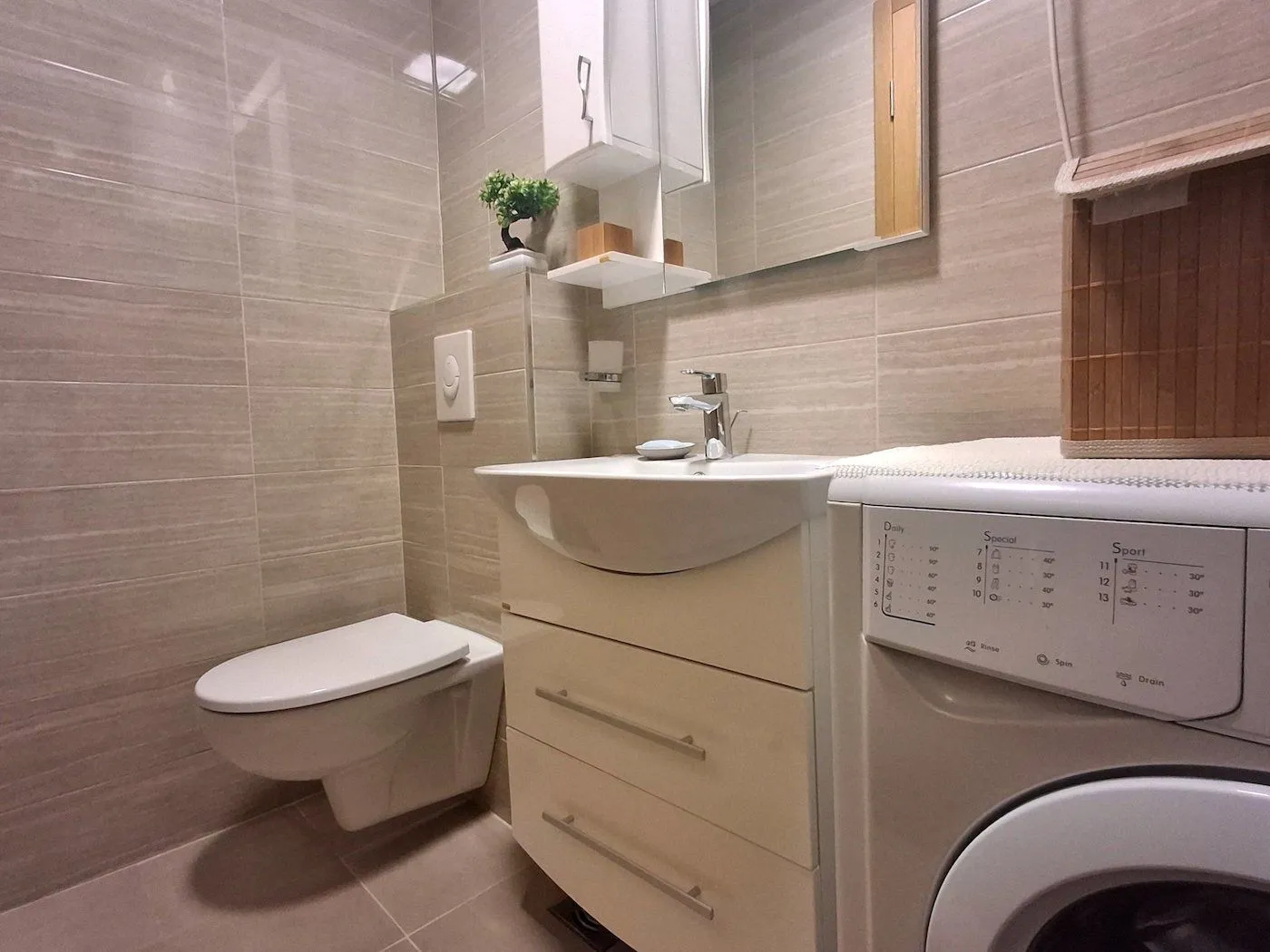 Modernly equipped bathroom with a washbasin, toilet bowl, and washing machine.