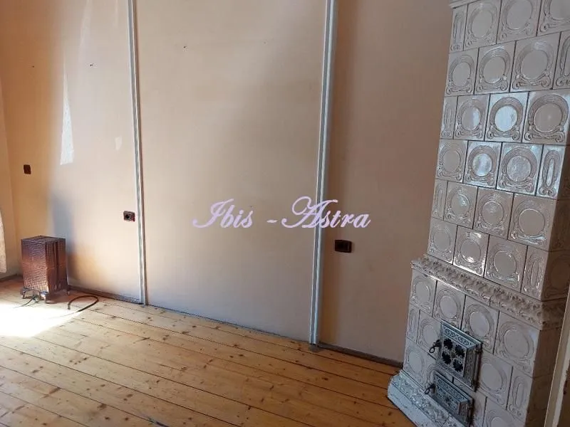 Empty room with wooden flooring and a tiled stove.
