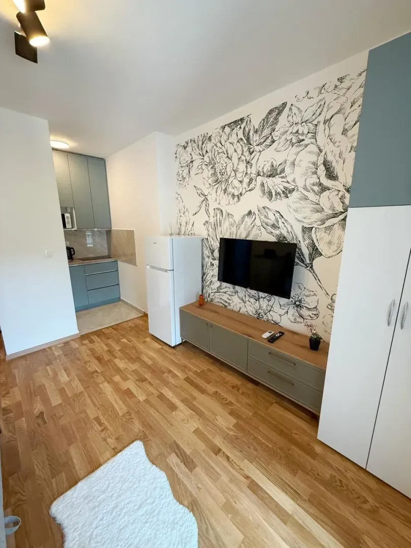 Living room with a TV, console, and floral wallpaper, with a view of a small kitchen.