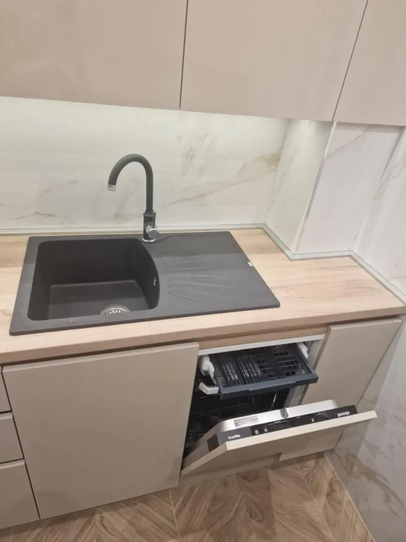 Deo kuhinje sa sudoperom i otvorenom mašinom za pranje sudova.