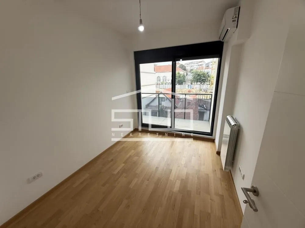 Prazna soba sa parketom i izlazom na balkon.
