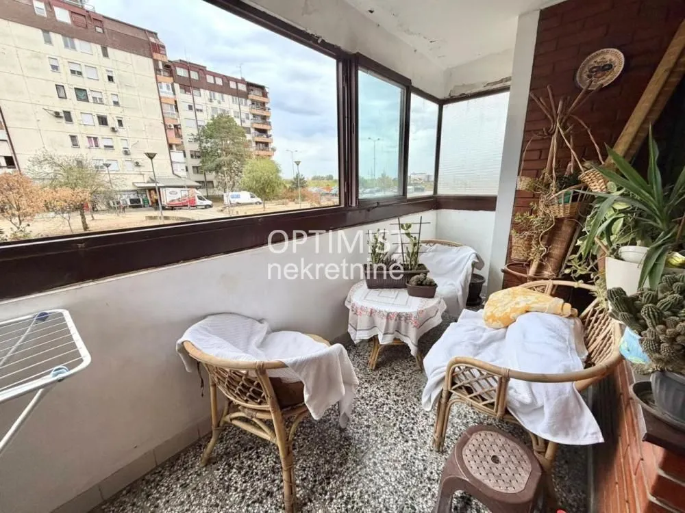 Zastakljeni balkon sa garniturom za sedenje i pogledom na okolne zgrade.