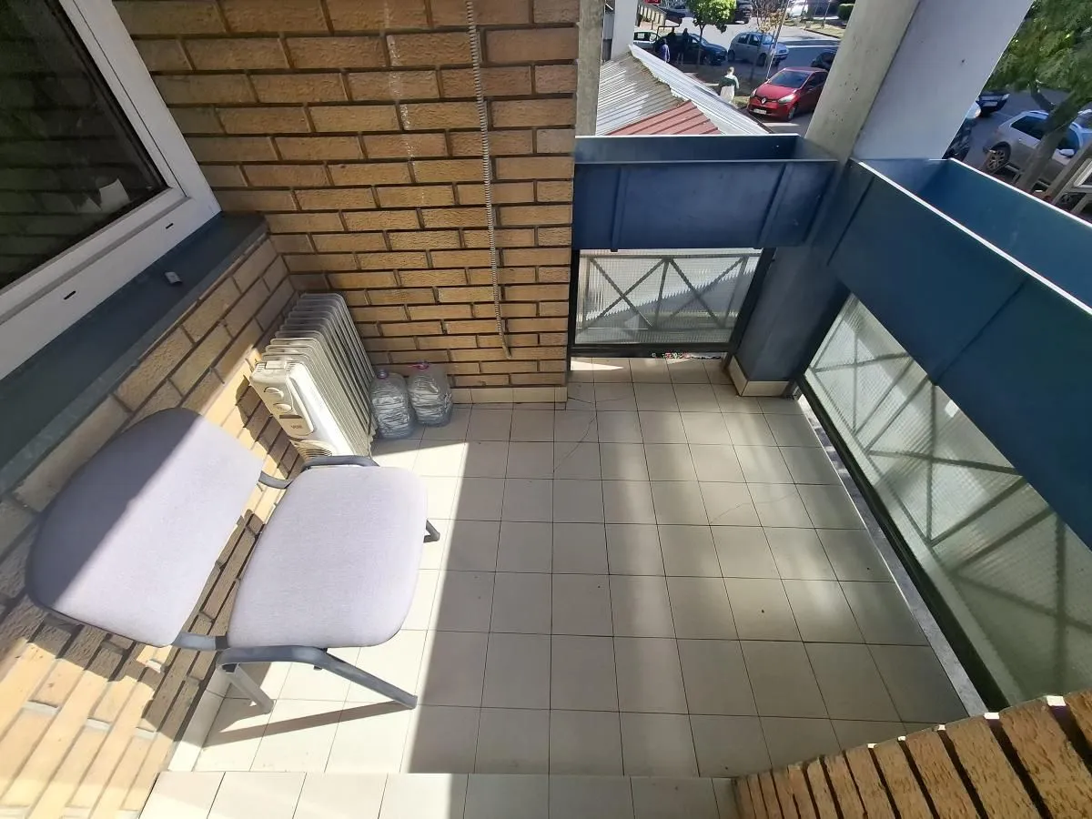 Manji popločani balkon sa stolicom i radijatorom.