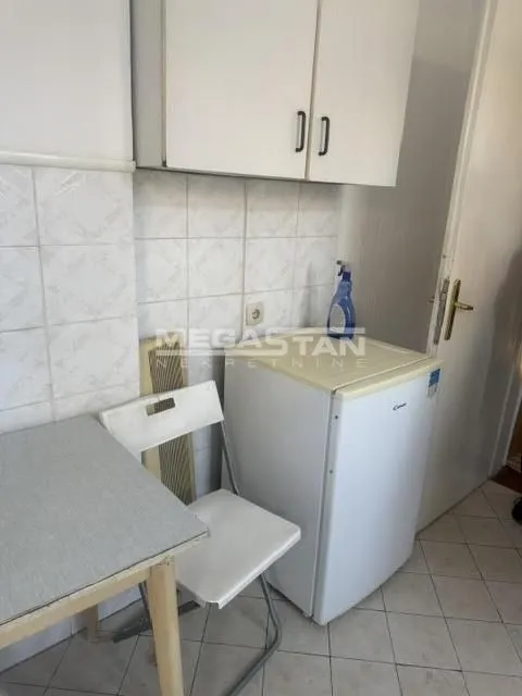 Manja kuhinja sa elementima, malim frižiderom i stolom sa stolicom.