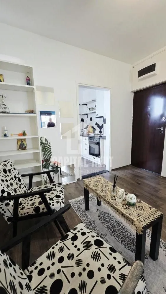 Living room with armchairs, a coffee table, and a shelving unit, with a view of the kitchen.