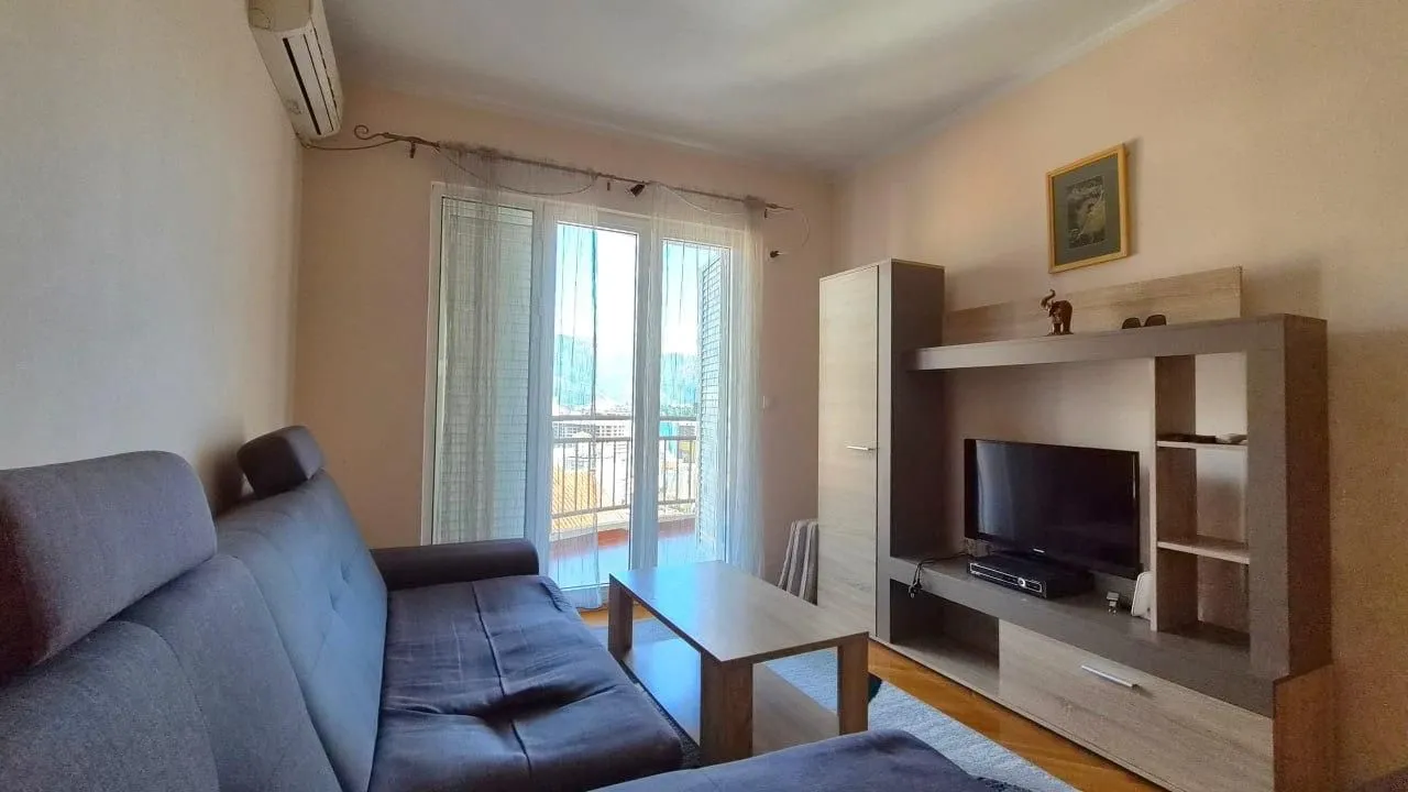 Dnevna soba sa garniturom, TV komodom i izlazom na terasu.