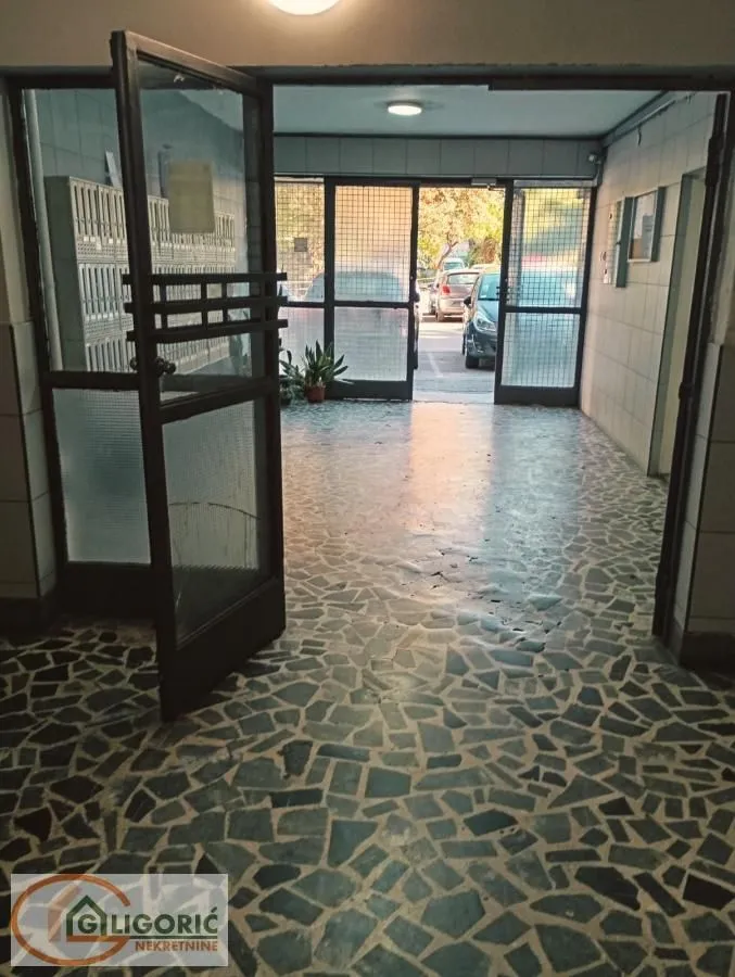 Ulaz u zgradu sa staklenim vratima i popločanim podom.