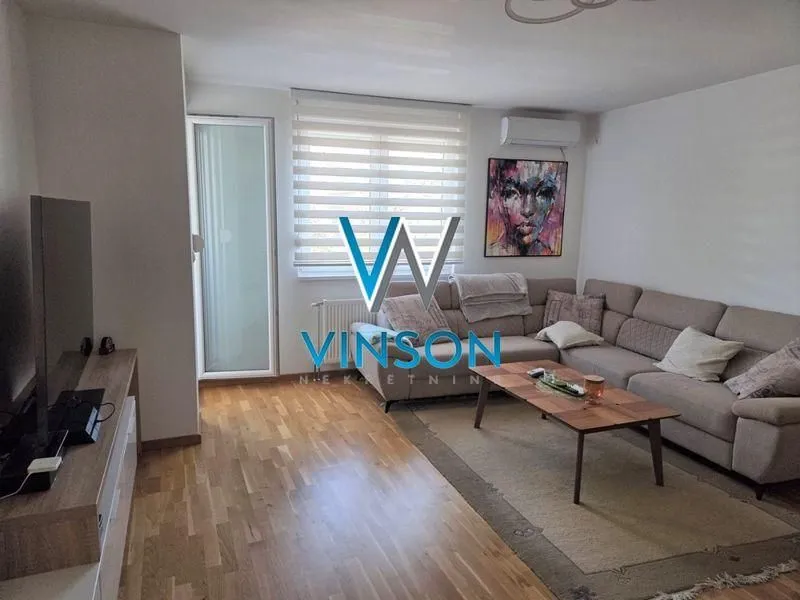 Dnevna soba sa ugaonom garniturom, stočićem i televizorom.