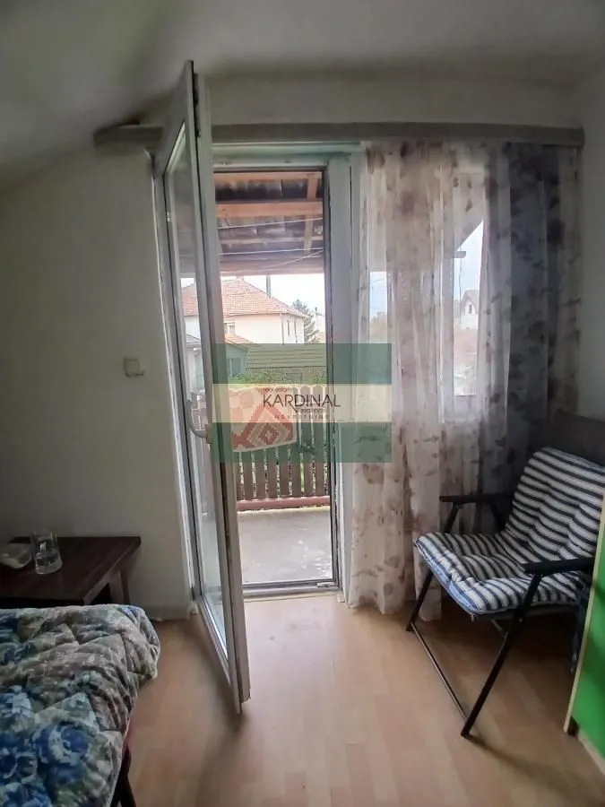 Manja soba sa krevetom, foteljom i izlazom na terasu.