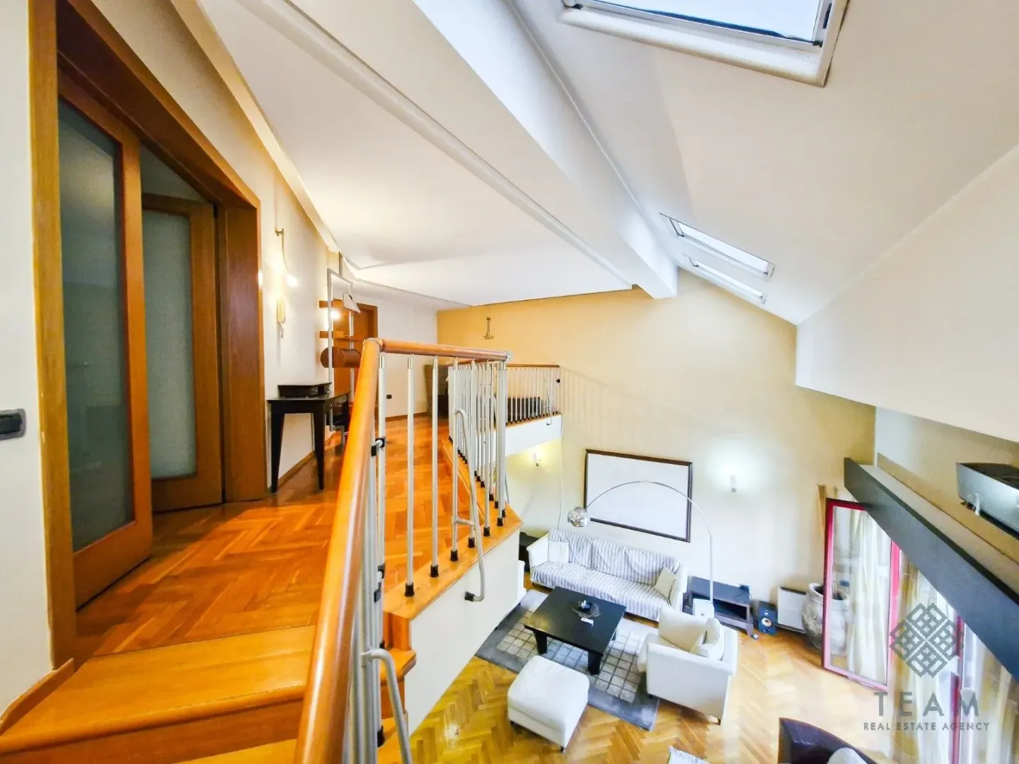 Pogled sa galerije na prostrani dnevni boravak sa drvenim podovima i visokim plafonom.