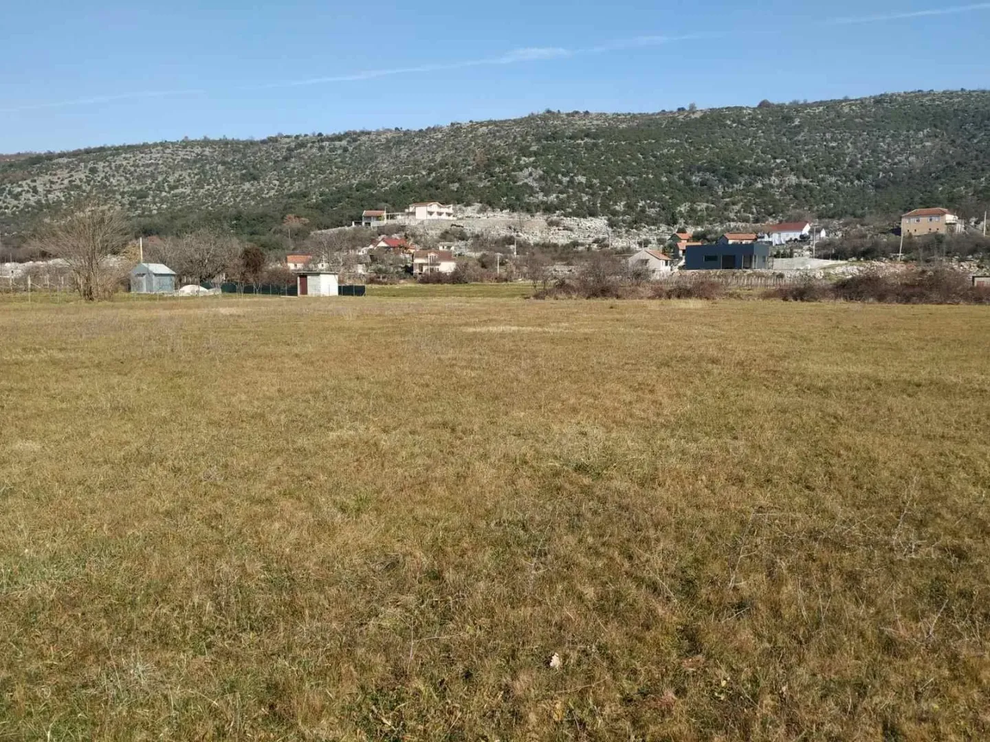 Pogled na prostrano ravno zemljište i okolno naselje u podnožju brda.