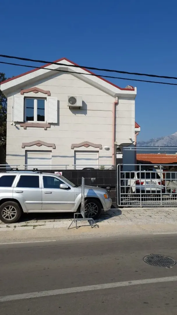 Spoljašnjost dvospratne kuće sa dvorištem i parkiranim automobilom.
